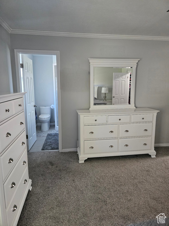 Unfurnished bedroom featuring dark colored carpet, ornamental molding, and ensuite bath