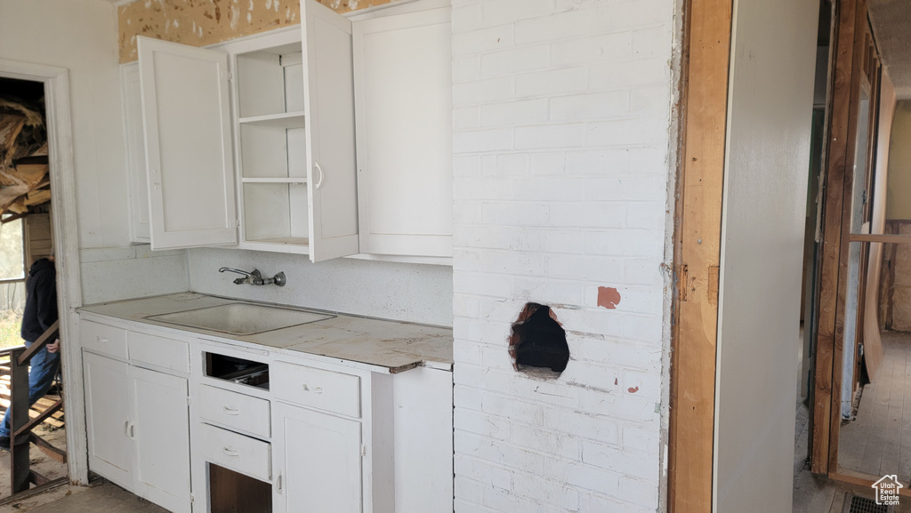 Kitchen featuring white cabinets, brick wall, and sink