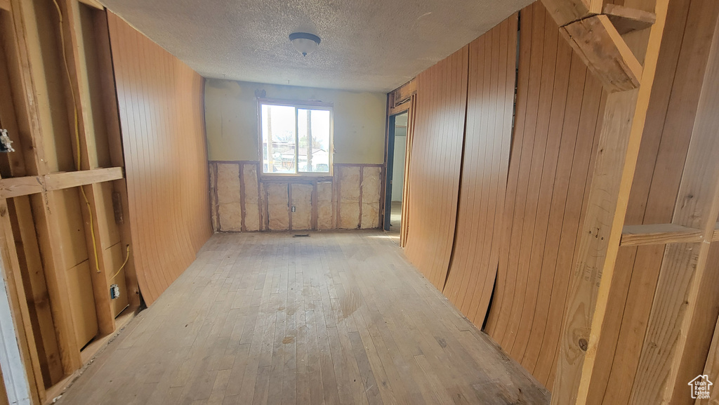 Corridor featuring wooden walls, light hardwood / wood-style flooring, and a textured ceiling
