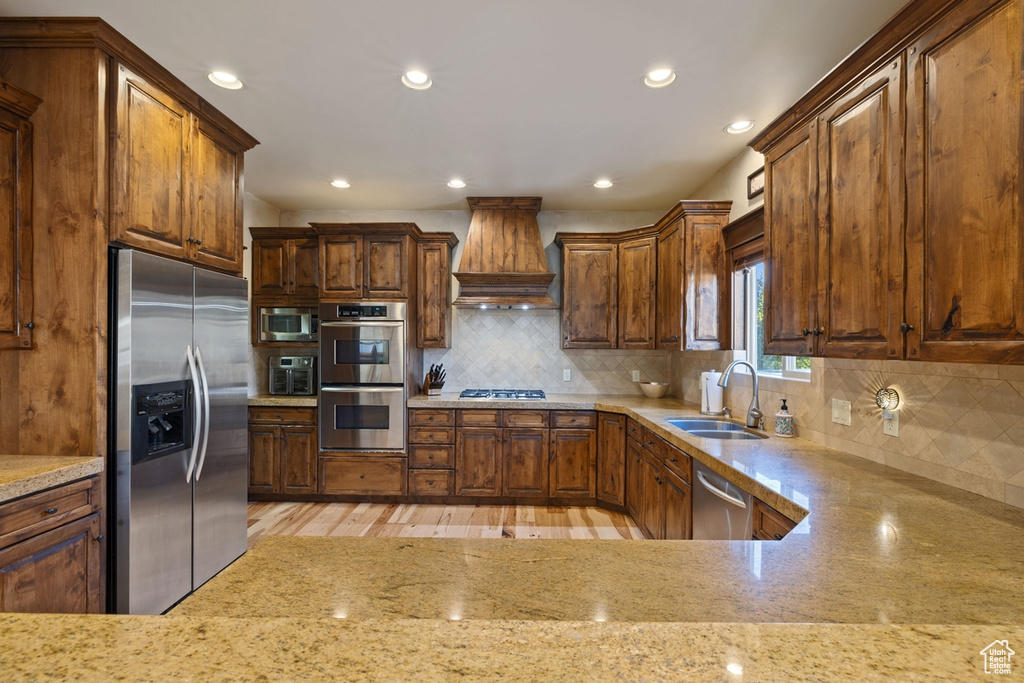 Kitchen featuring light stone counters, stainless steel appliances, sink, light hardwood / wood-style floors, and custom exhaust hood