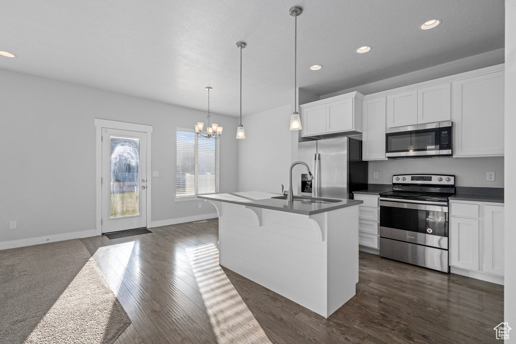 Kitchen featuring white cabinets, appliances with stainless steel finishes, hanging light fixtures, and a kitchen island with sink