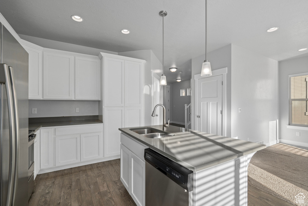 Kitchen with sink, appliances with stainless steel finishes, an island with sink, white cabinets, and dark hardwood / wood-style flooring