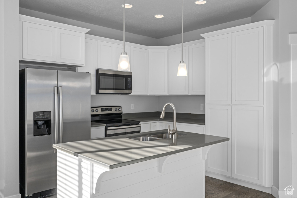 Kitchen with dark wood-type flooring, sink, pendant lighting, appliances with stainless steel finishes, and white cabinetry