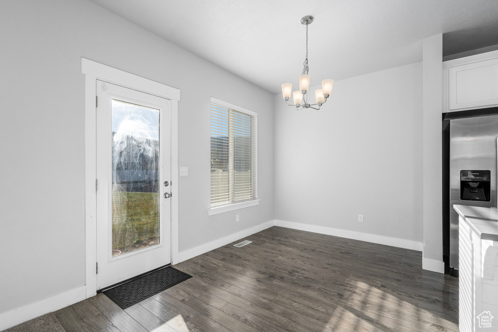 Unfurnished dining area featuring dark hardwood / wood-style flooring and a notable chandelier