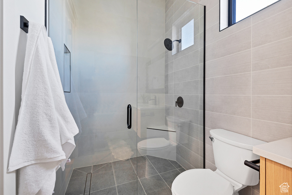 Bathroom with toilet, a shower with door, tile walls, tile patterned flooring, and vanity