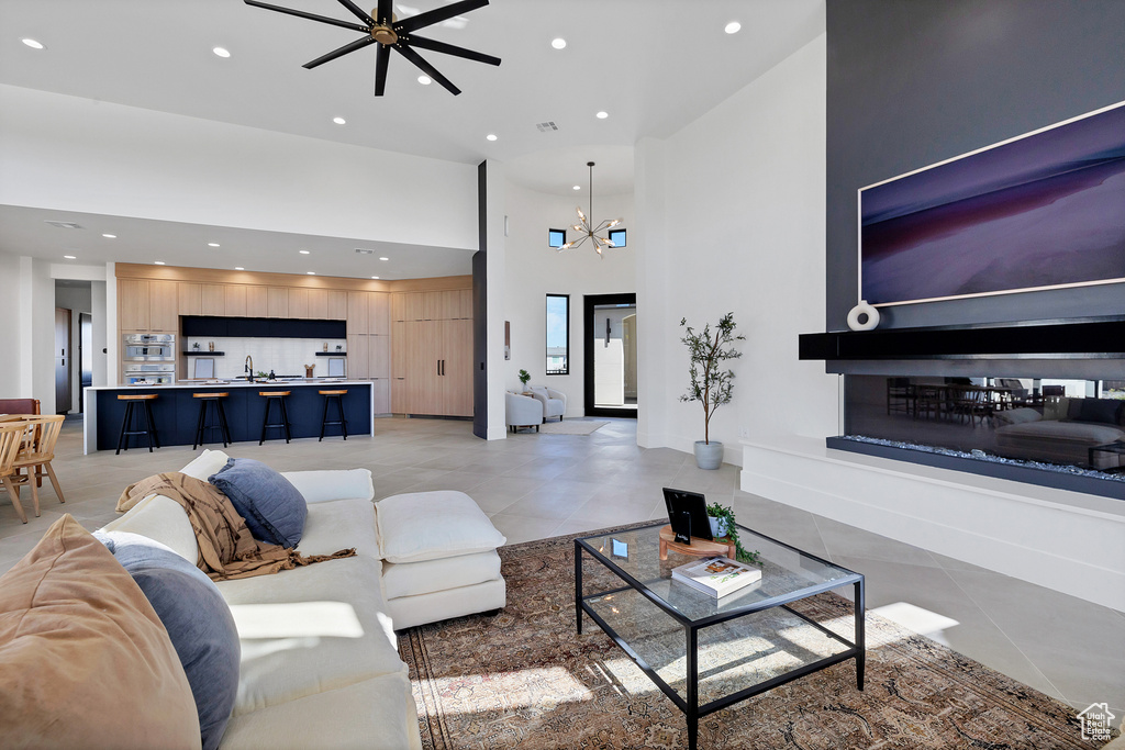 Living room with ceiling fan with notable chandelier, sink, light tile patterned floors, and a towering ceiling