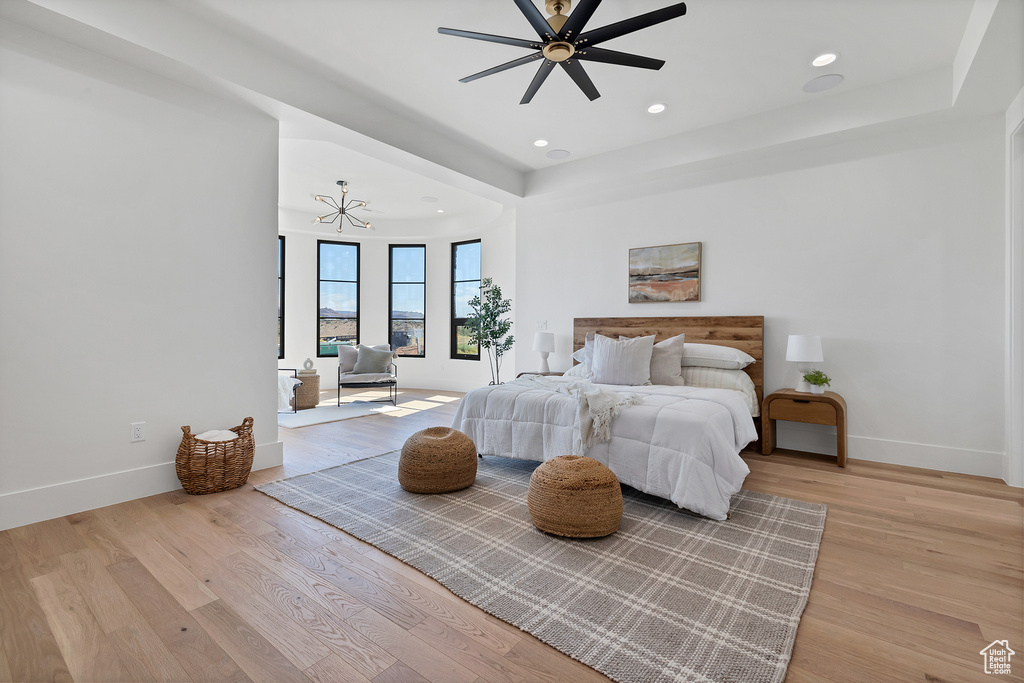 Bedroom with light hardwood / wood-style floors and ceiling fan with notable chandelier