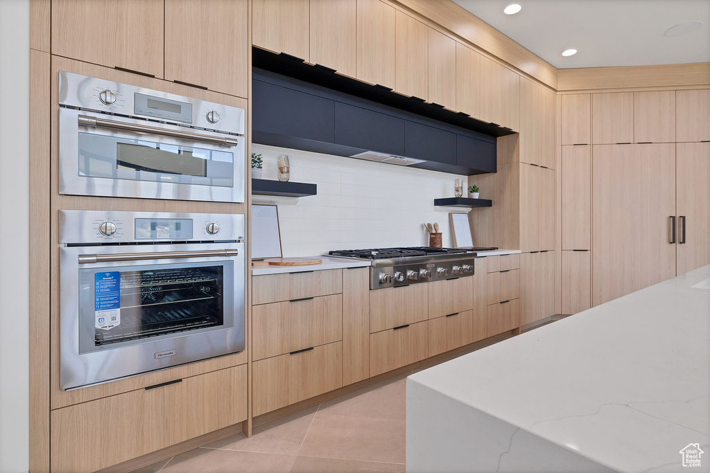 Kitchen featuring stainless steel appliances, light brown cabinetry, light tile patterned floors, and backsplash