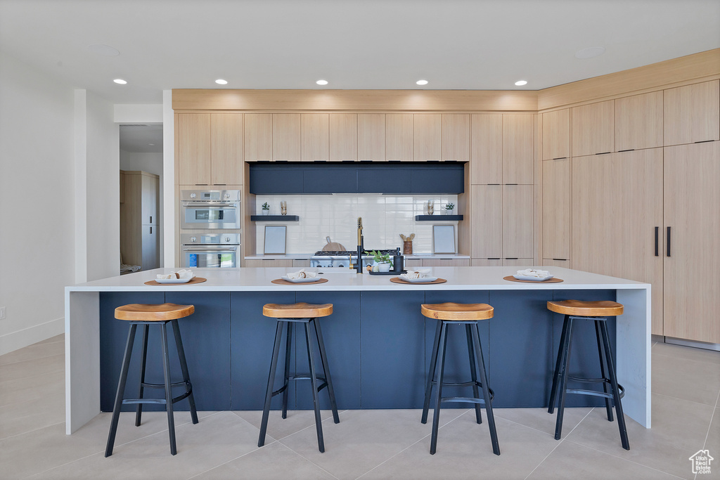 Kitchen featuring a kitchen bar, decorative backsplash, a large island with sink, and light brown cabinets