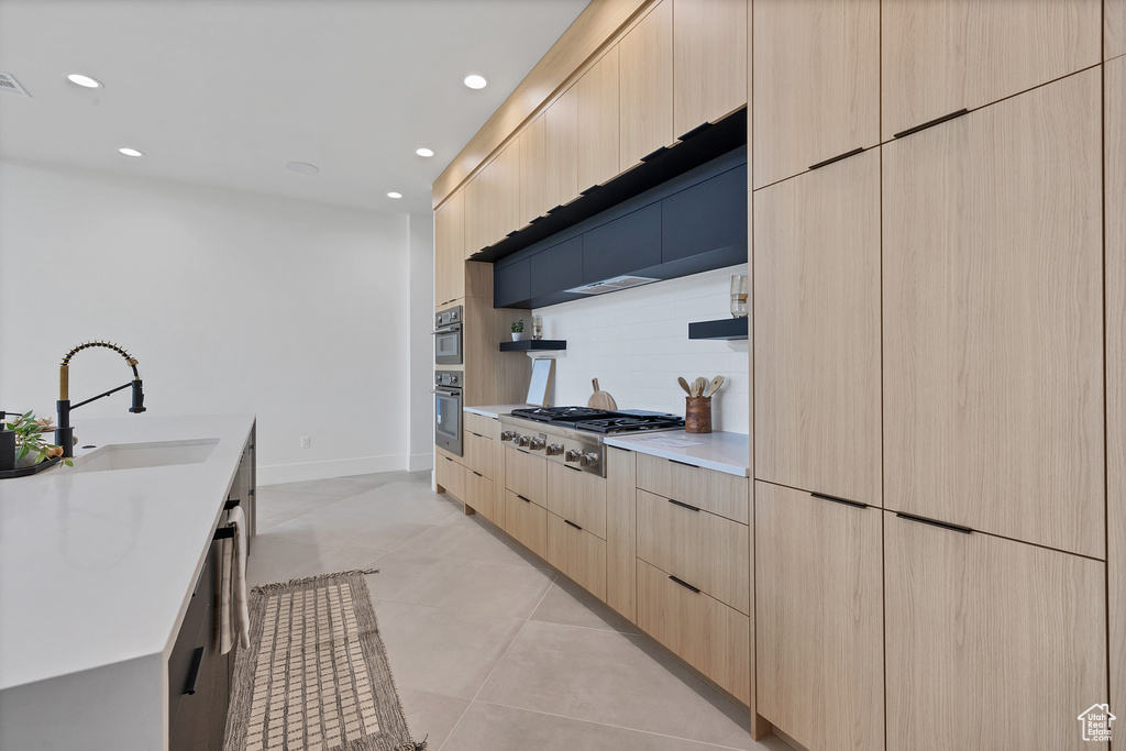 Kitchen featuring light tile patterned flooring, sink, appliances with stainless steel finishes, light brown cabinetry, and decorative backsplash