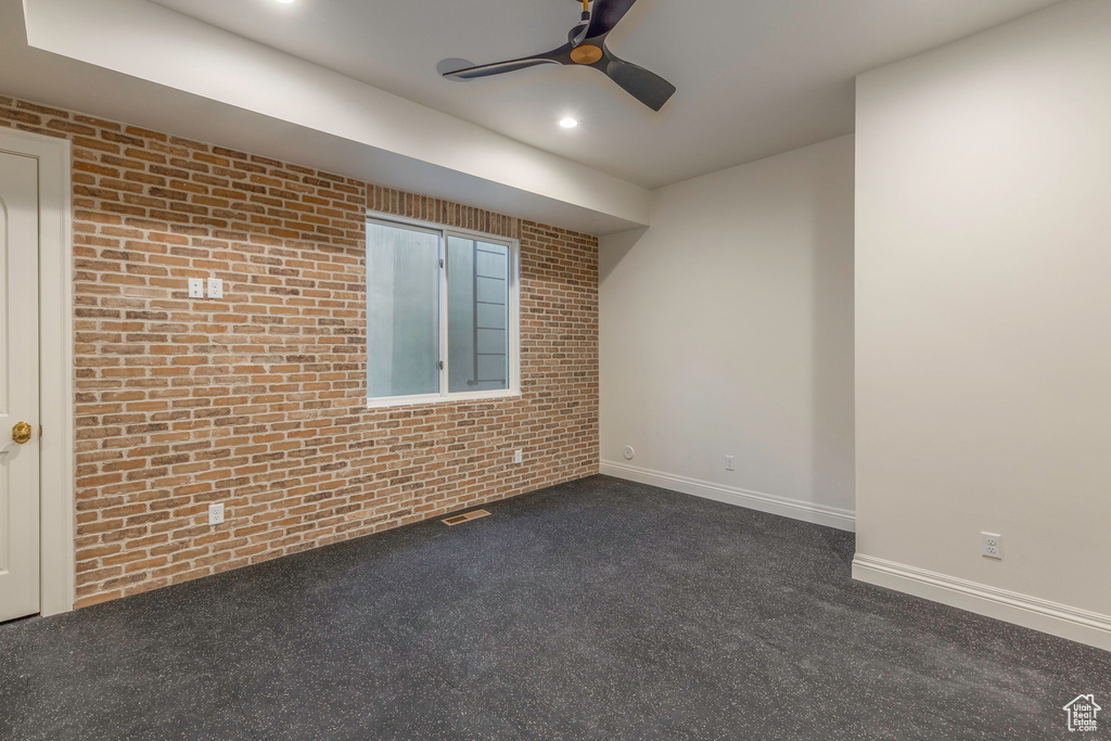 Carpeted empty room with brick wall and ceiling fan