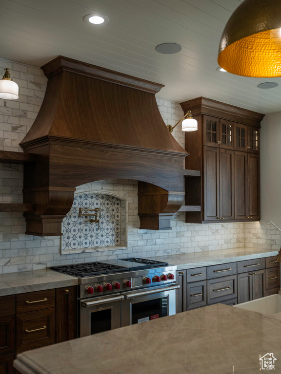 Kitchen featuring backsplash, light stone counters, custom range hood, and range with two ovens