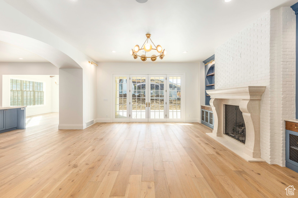 Unfurnished living room with light wood-type flooring, a chandelier, french doors, and a large fireplace