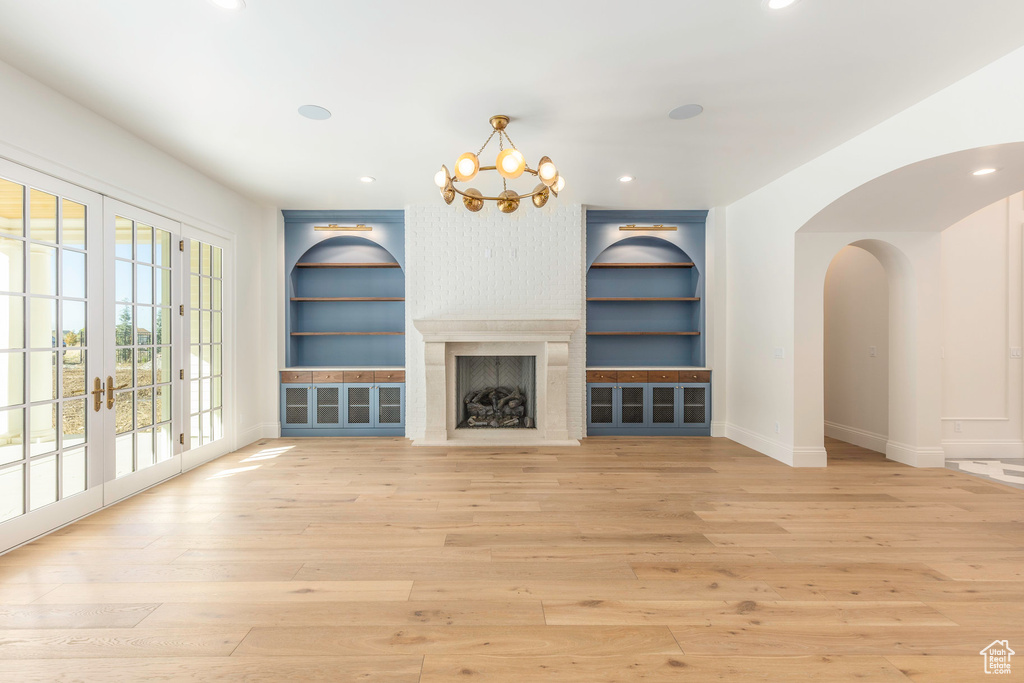 Unfurnished living room with built in shelves, light wood-type flooring, french doors, and an inviting chandelier