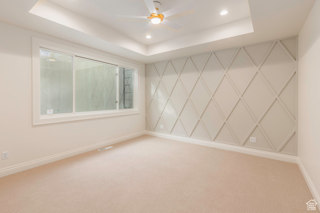 Empty room with carpet, ceiling fan, and a raised ceiling