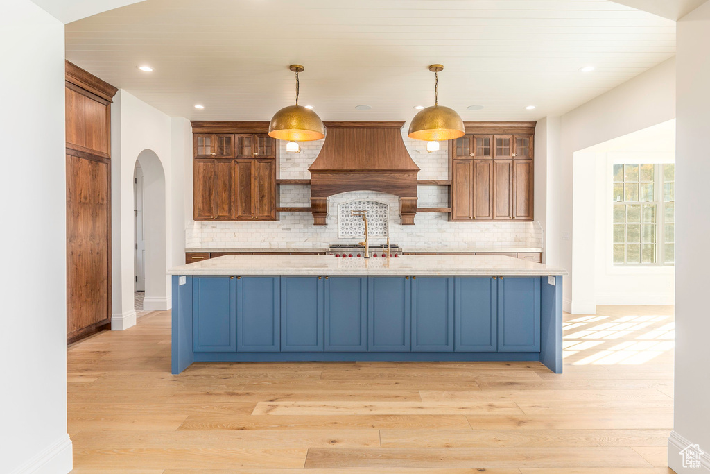 Kitchen with decorative backsplash, light wood-type flooring, decorative light fixtures, and custom range hood