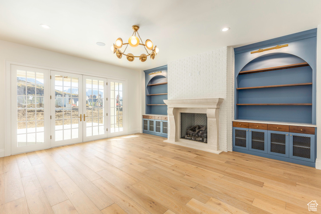 Unfurnished living room featuring a large fireplace, hardwood / wood-style floors, a chandelier, built in features, and french doors