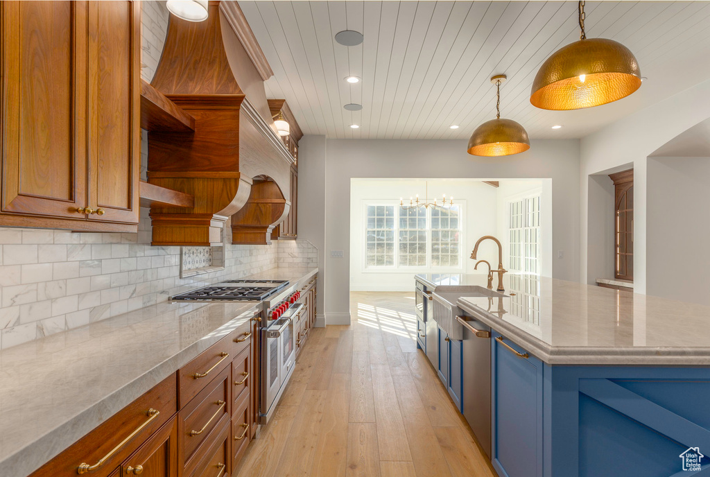 Kitchen with range with two ovens, sink, a kitchen island with sink, pendant lighting, and light hardwood / wood-style flooring