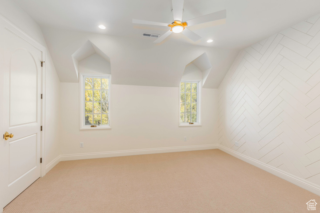 Additional living space with ceiling fan, vaulted ceiling, light colored carpet, and a healthy amount of sunlight