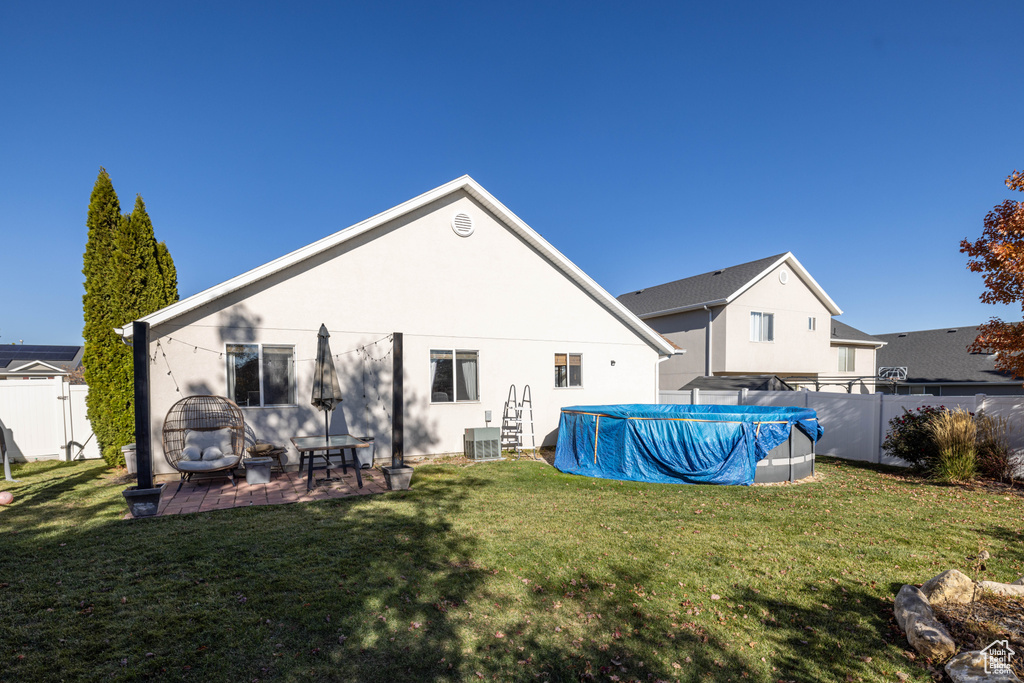 Rear view of property featuring central air condition unit, a lawn, a covered pool, and a patio