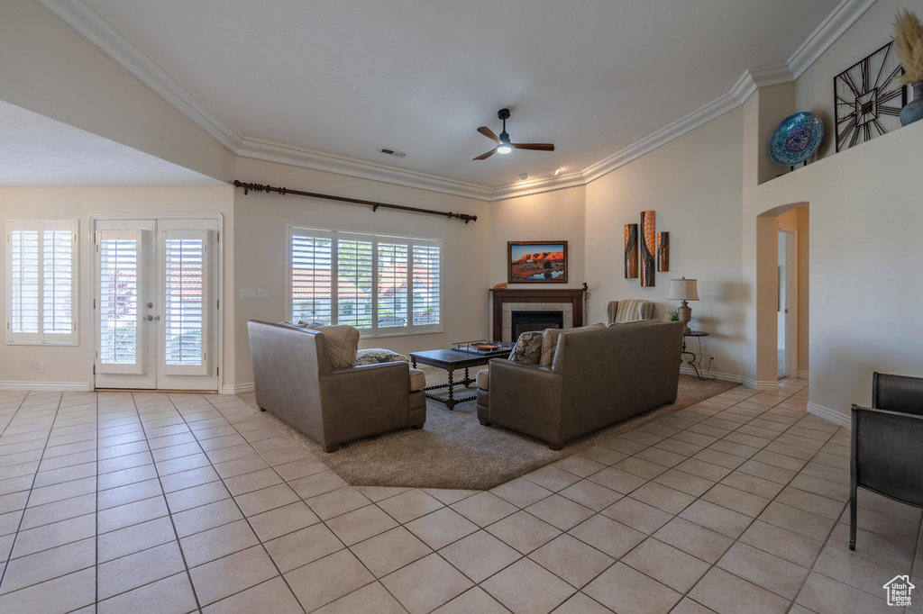 Living area featuring light tile patterned flooring, a ceiling fan, a tiled fireplace, crown molding, and arched walkways