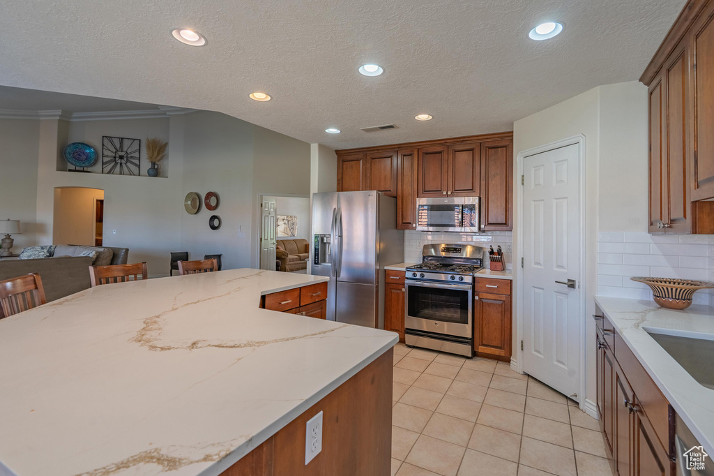 Kitchen featuring appliances with stainless steel finishes, open floor plan, decorative backsplash, light tile patterned floors, and light stone countertops