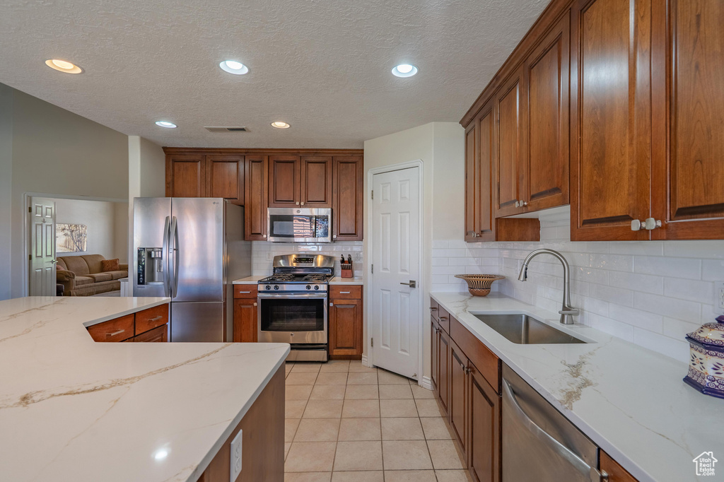 Kitchen featuring appliances with stainless steel finishes, a sink, decorative backsplash, light tile patterned floors, and brown cabinetry