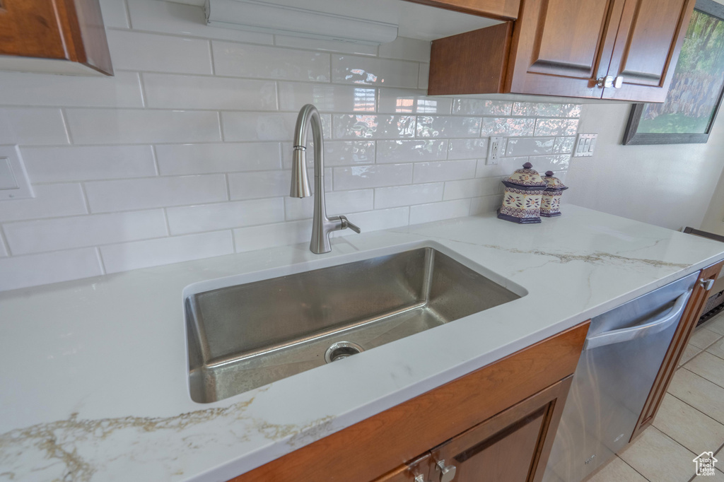 Kitchen featuring a sink, backsplash, brown cabinets, dishwasher, and light stone counters