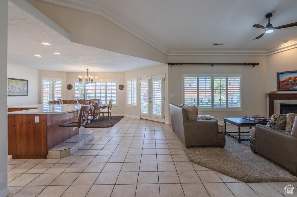 Living area with light tile patterned flooring, a tile fireplace, a ceiling fan, crown molding, and a chandelier