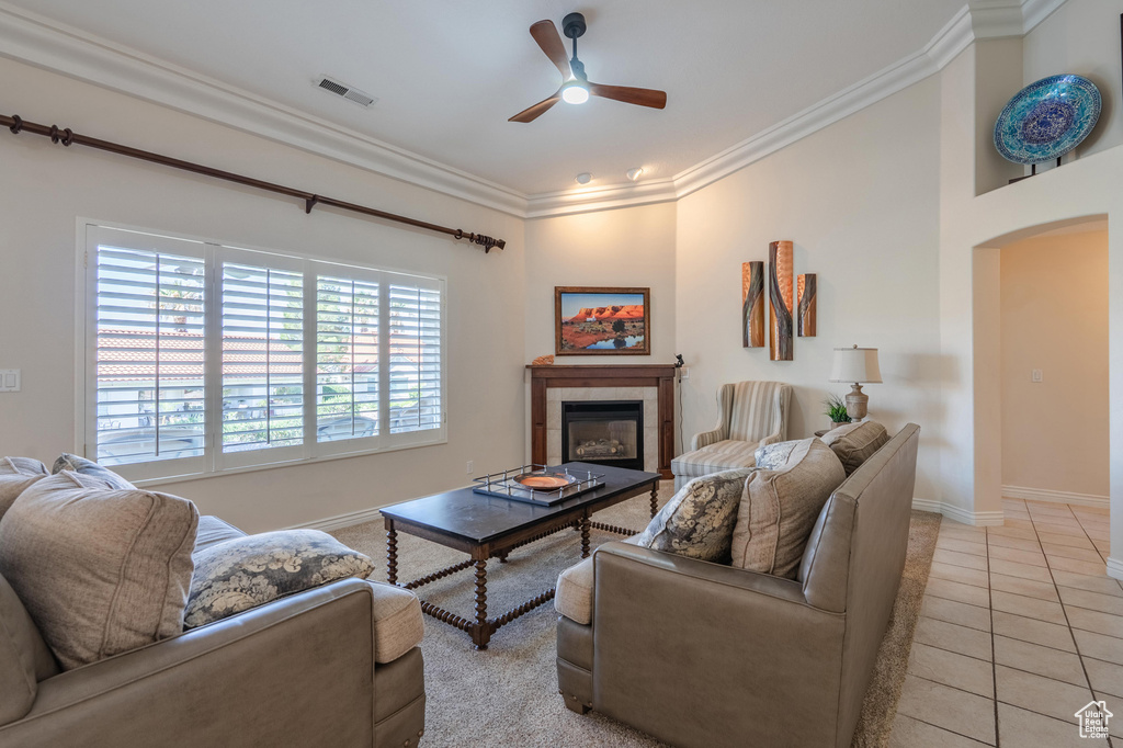 Living room with ceiling fan, crown molding, baseboards, light tile patterned flooring, and a tiled fireplace