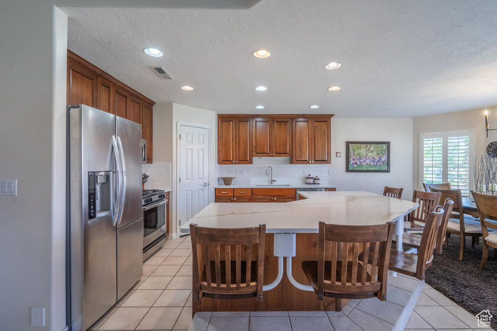 Kitchen featuring appliances with stainless steel finishes, a sink, recessed lighting, brown cabinets, and tasteful backsplash