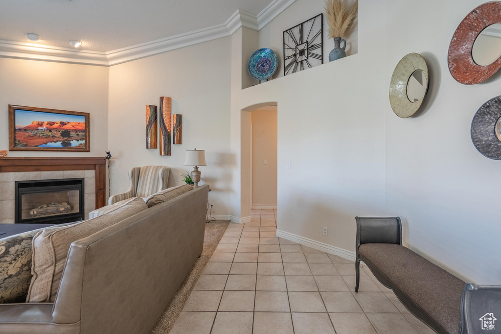 Living area with arched walkways, crown molding, light tile patterned floors, a tiled fireplace, and baseboards