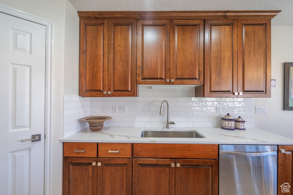 Kitchen featuring dishwasher, a sink, backsplash, brown cabinets, and light stone counters