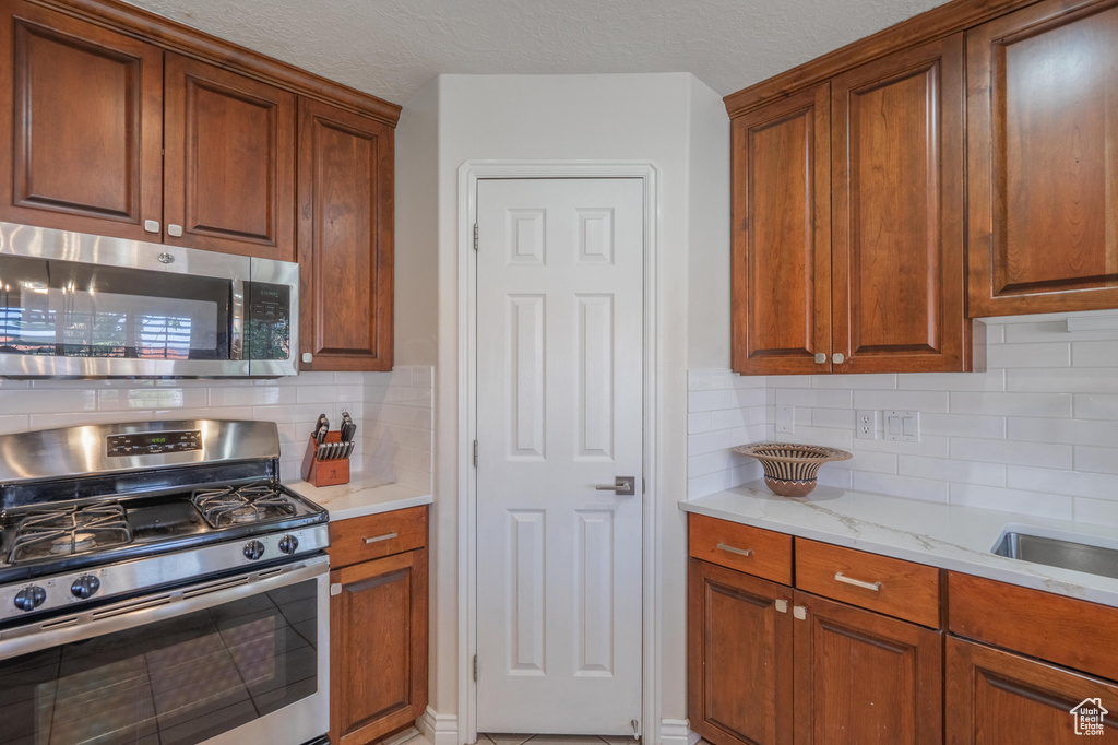 Kitchen with stainless steel appliances, backsplash, brown cabinetry, and light stone countertops