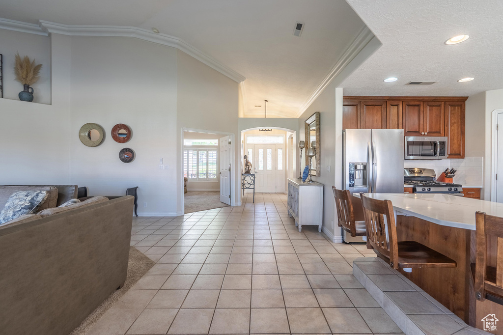 Kitchen featuring appliances with stainless steel finishes, crown molding, light countertops, baseboards, and a breakfast bar area