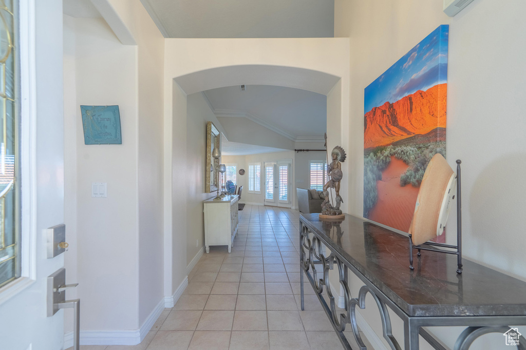 Hallway with arched walkways, ornamental molding, light tile patterned flooring, and baseboards