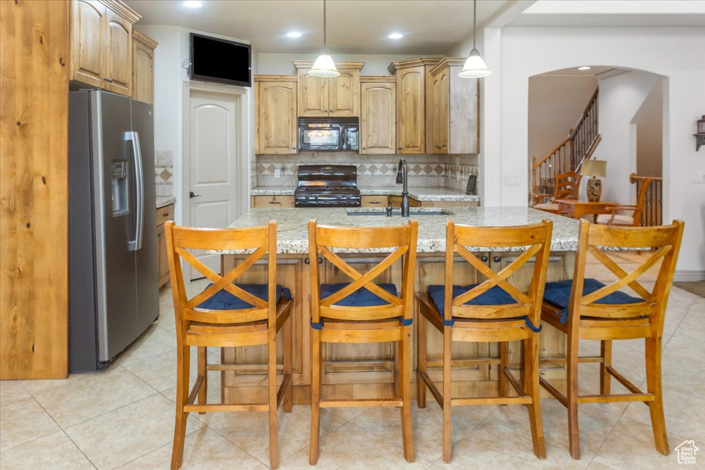 Kitchen featuring black appliances, light stone counters, backsplash, sink, and a breakfast bar area