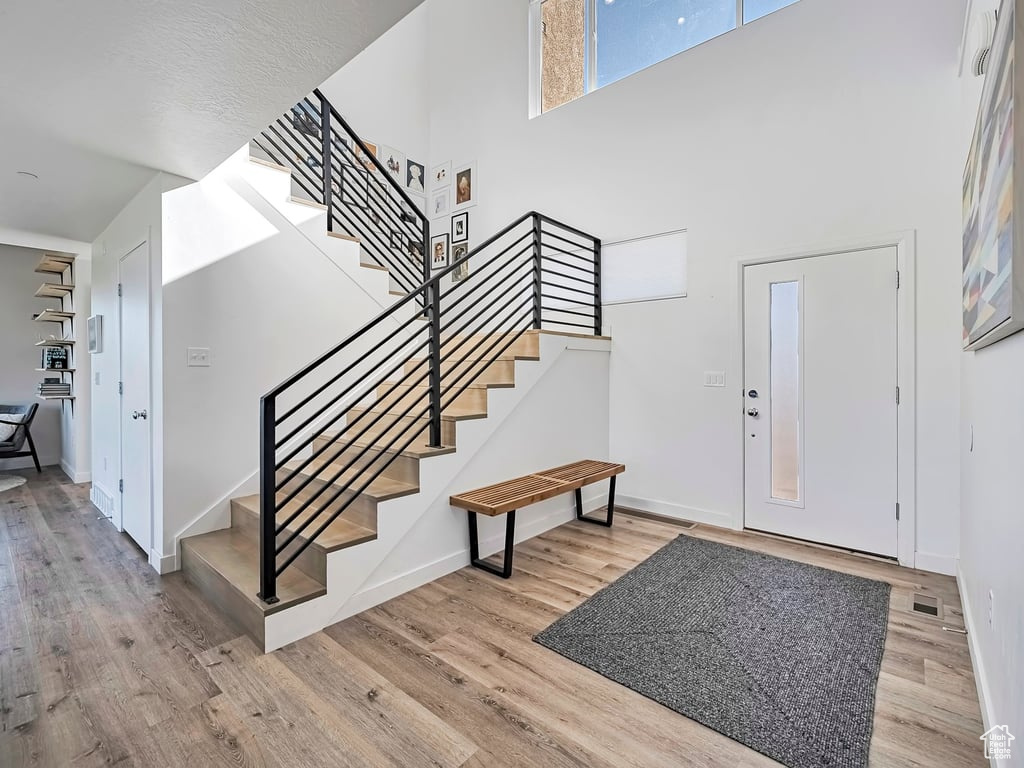 Foyer with wood finished floors, stairs, and a towering ceiling