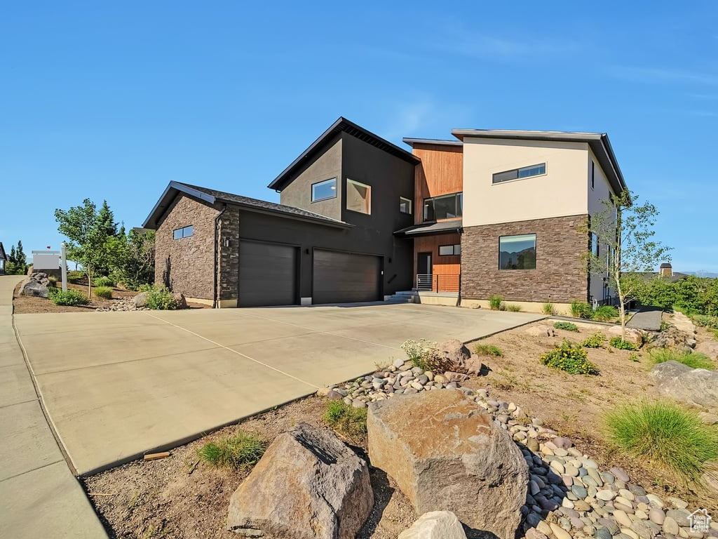 View of front of home with concrete driveway, an attached garage, stone siding, and stucco siding