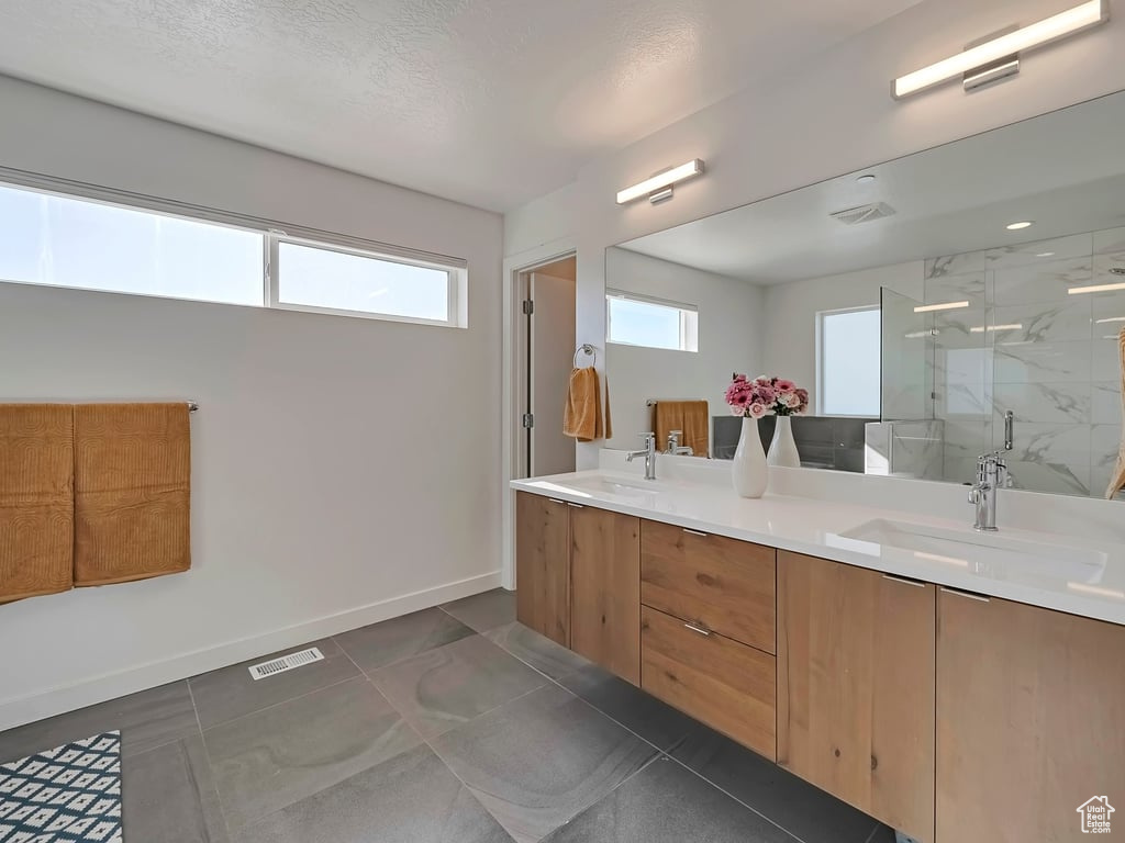 Full bathroom with a marble finish shower, double vanity, tile patterned flooring, and a textured ceiling