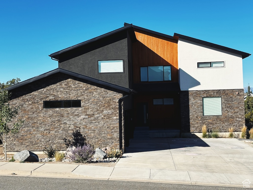 Modern home featuring stone siding, concrete driveway, stucco siding, and a garage