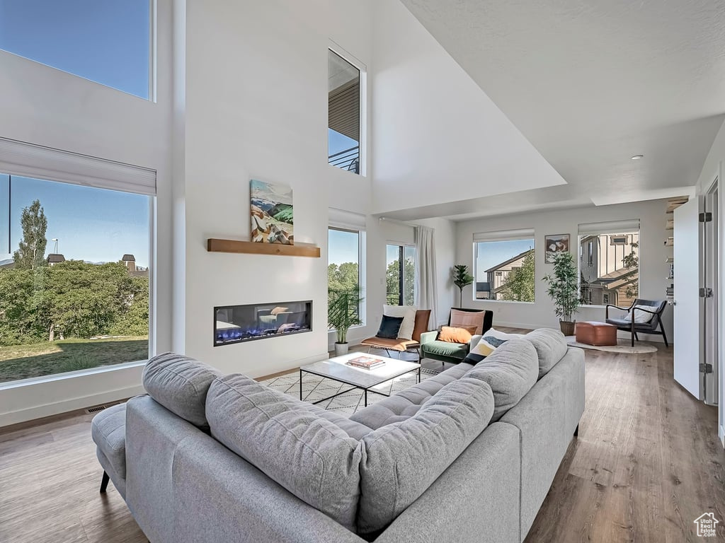Living area featuring wood finished floors, a glass covered fireplace, and a towering ceiling