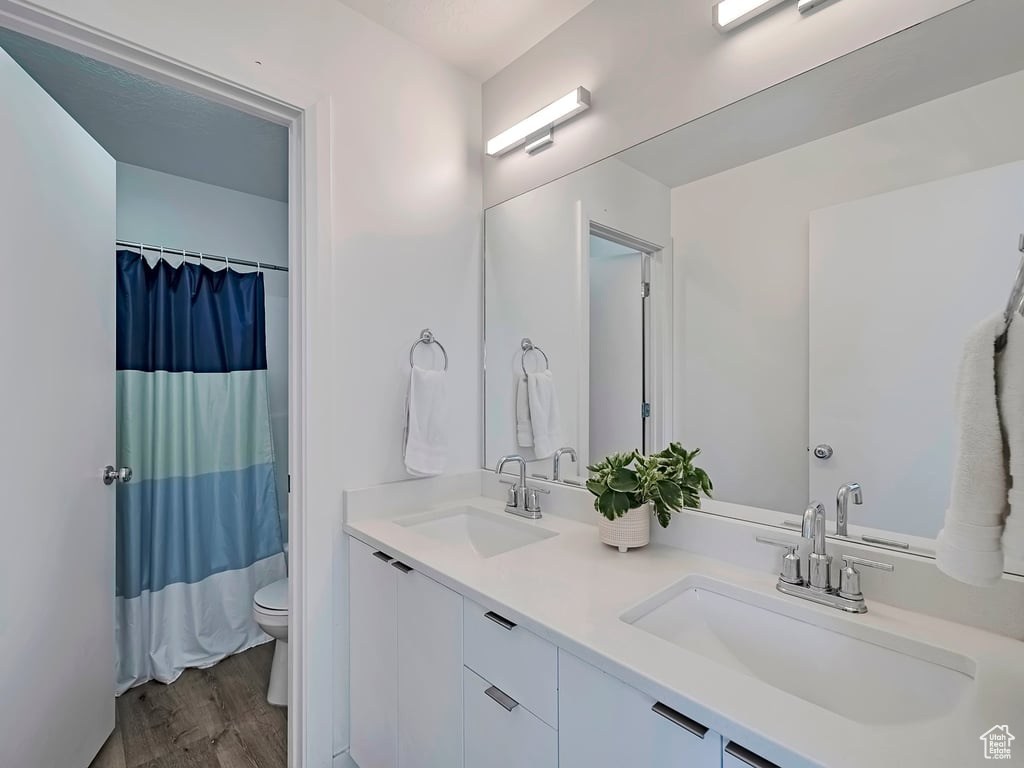 Full bathroom with double vanity, wood finished floors, and a shower with shower curtain