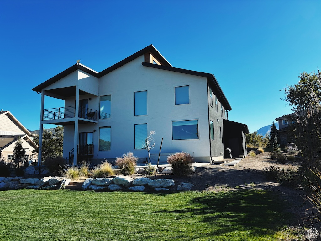 Rear view of house featuring a balcony, stucco siding, and a lawn