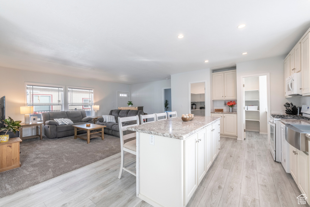 Kitchen with white cabinets, a breakfast bar area, light carpet, a kitchen island, and white appliances