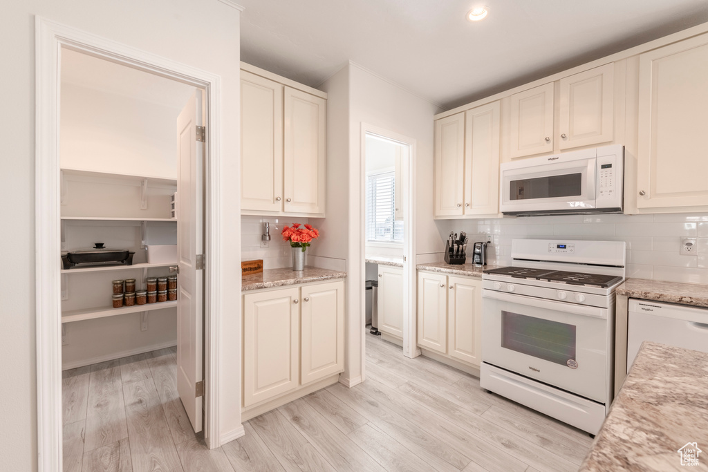 Kitchen with backsplash, white appliances, light stone countertops, and light wood-type flooring