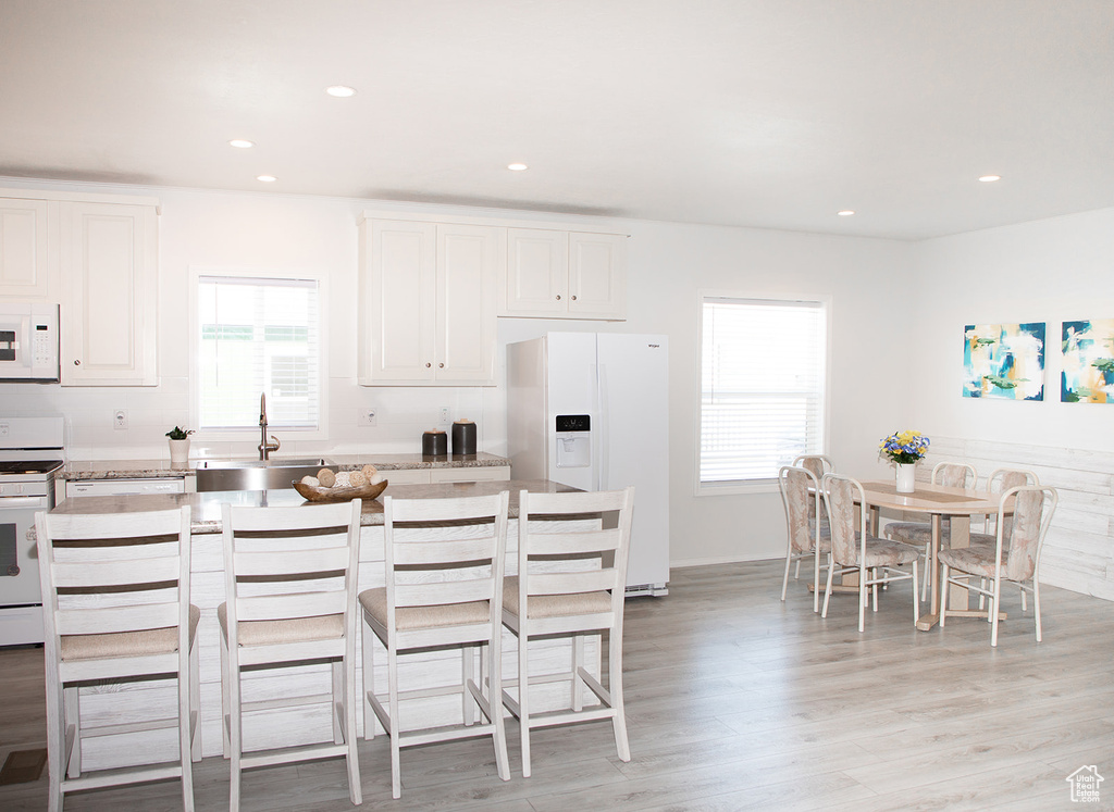 Kitchen featuring white cabinetry, sink, light hardwood / wood-style floors, white appliances, and a center island