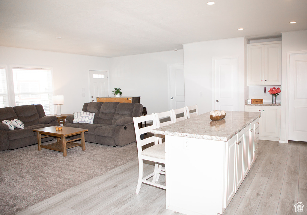 Kitchen featuring a kitchen island, white cabinetry, light colored carpet, and a kitchen breakfast bar