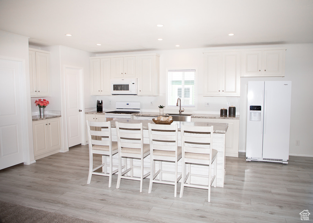 Kitchen featuring white cabinetry, sink, white appliances, and a kitchen island