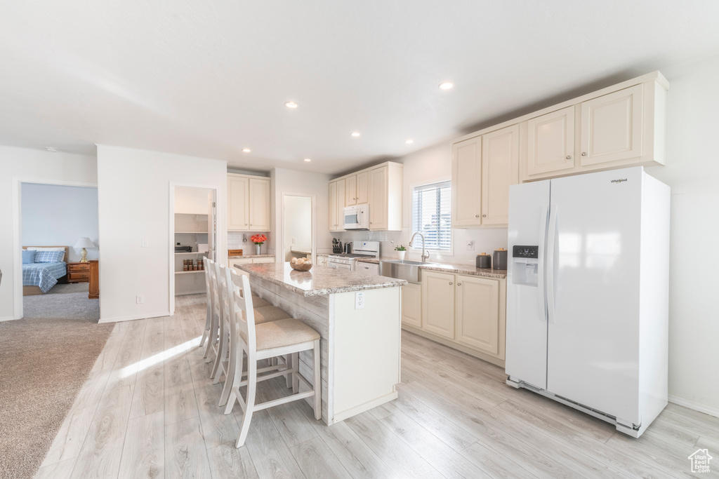 Kitchen featuring light hardwood / wood-style flooring, a center island, white appliances, and a breakfast bar area